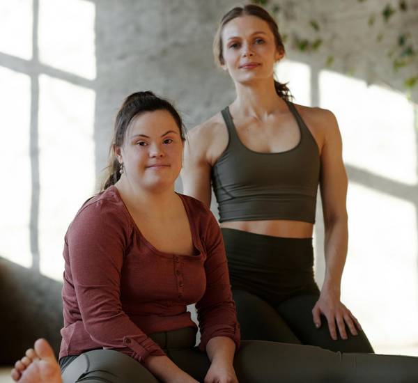 zwei junge Frauen sitzen in einem Sportraum und blicken zur Kamera